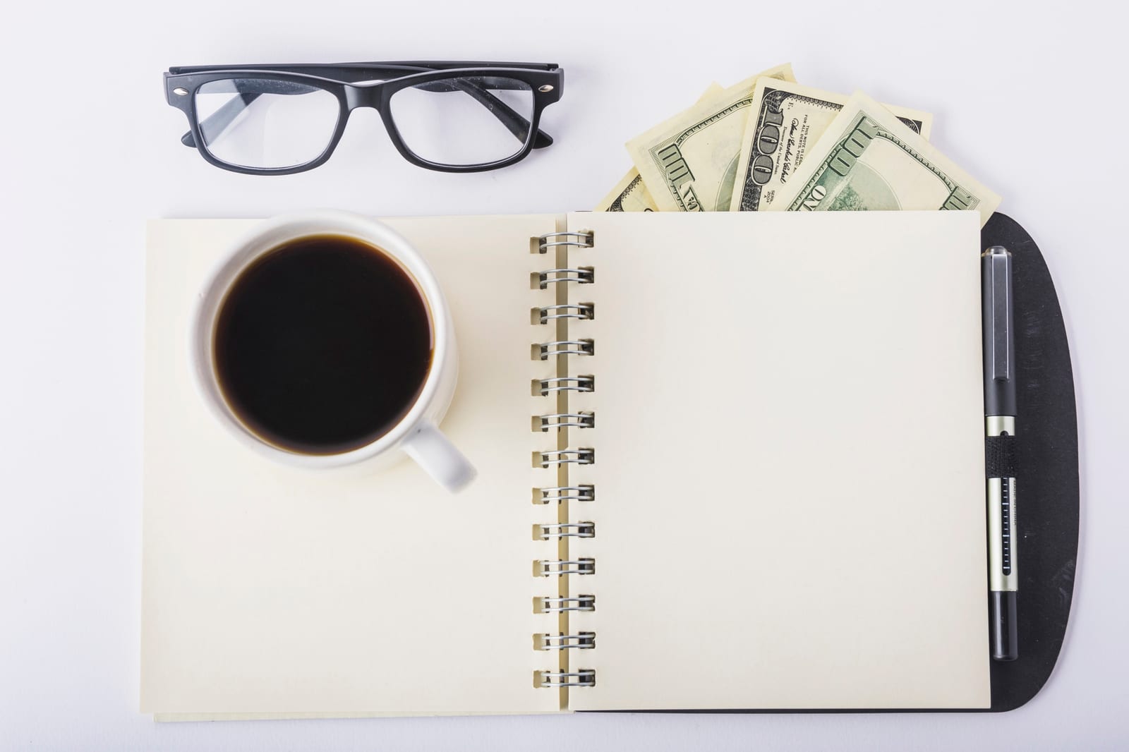 Una tazza di caffè accanto a un quaderno di appunti e a un paio di occhiali su una scrivania